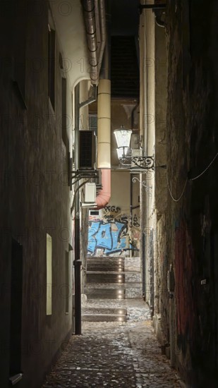 Narrow, illuminated alley at night with stairs lined with graffiti and old architecture, Ljubljana,