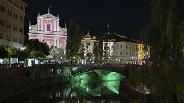 River with illuminated bridge and historic buildings in an atmospheric night view, Ljubljana,