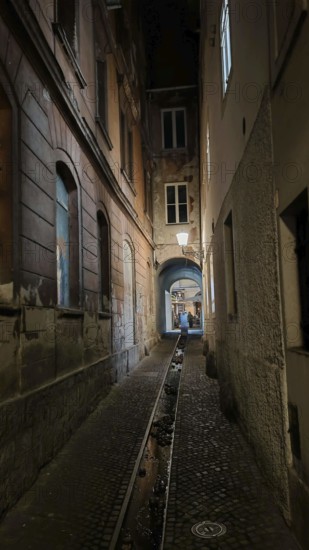 Dark, narrow alley at night with cobblestones and dim lantern light, urban atmosphere, Ljubljana,