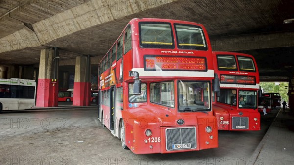 Classic red double-decker bus under a large concrete shelter at a bus station, Skopje, North