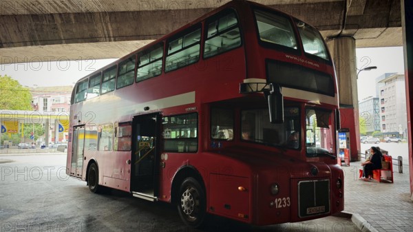 Classic red double-decker bus at a bus stop in an urban environment under a bridge, Skopje, North