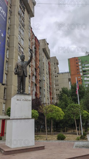 Bill Clinton statue in front of an apartment block with surrounding trees and flagpoles, Pristina,