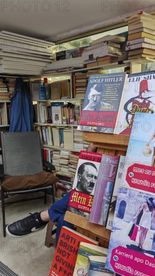 Bookshelves in an outdoor bookstore with various books, Mein Kampf, and an empty chair, Pristina,