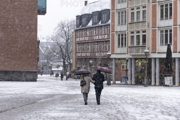 Two passers-by walk across Frankfurt's Römerberg with umbrellas. Heavy snowfalls have caused