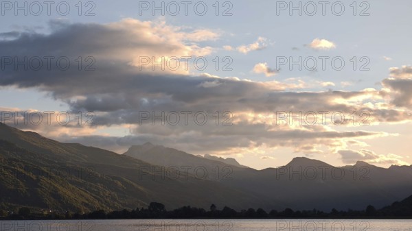 View of a mountain range with clouds glowing over a calm lake in the evening light, Plav Lake,