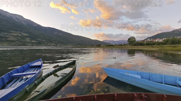 Three colorful boats on a calm lake at sunset surrounded by mountains and cloudy sky, Plav Lake,
