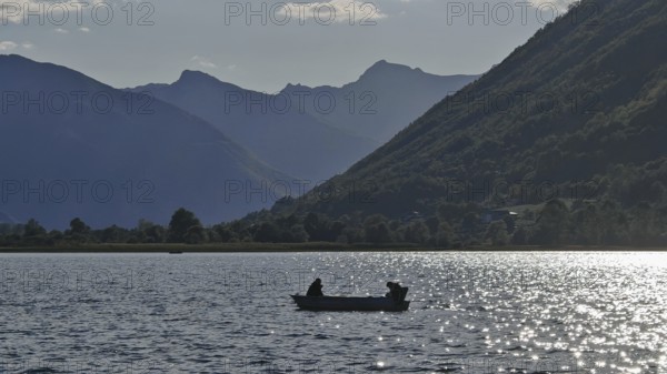 A boat with two people on a lake surrounded by mountain silhouettes in the evening light, Lake