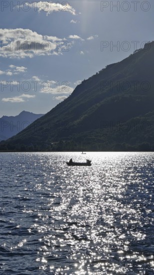 A lonely boat on a sparkling lake with mountains in the background and sunny atmosphere, Lake Plav,