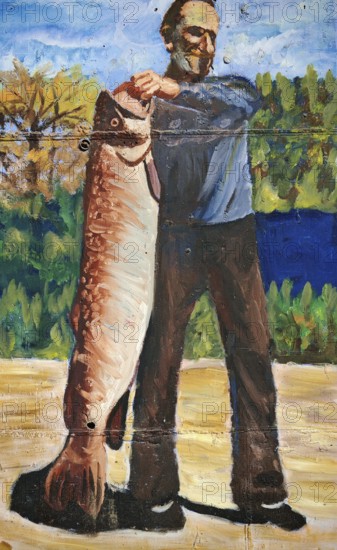 Painting of a man holding a big fish against a wooded background, Montenegro
