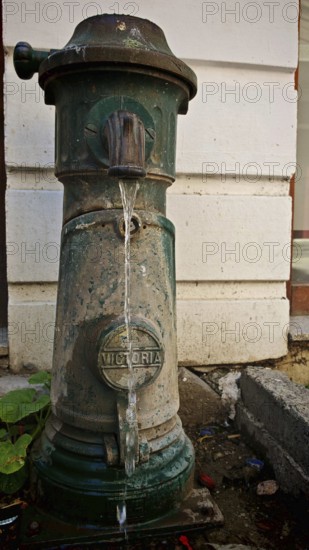 Old green hydrant with Victoria inscription with water flow in front of a wall, Kosovo
