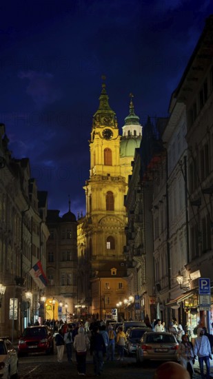 A magnificently illuminated church rises above a busy city street at night, Prague