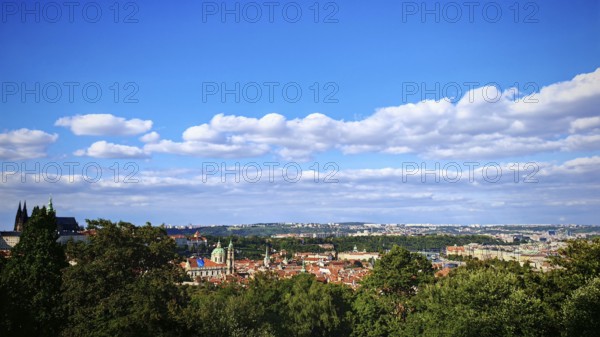 City panorama with distinctive buildings and green hills under a blue sky, view over Prague, Czech