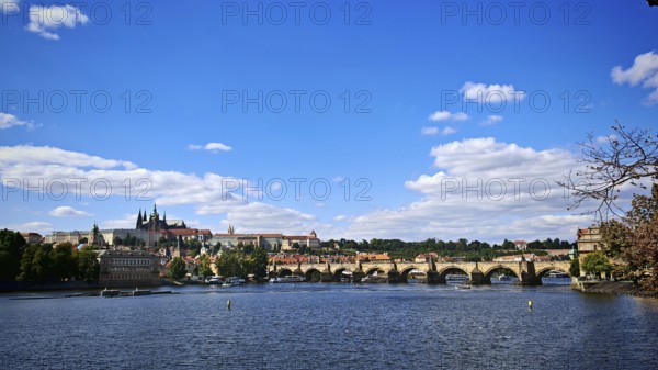 Panorama of a bridge and surrounding architecture along a river under a blue sky, Prague, Czech