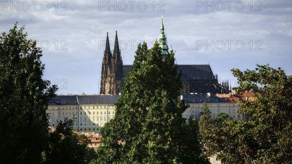 Gothic church between tall trees, cloudy sky in the background, view of Hradcany, Prague, Czech