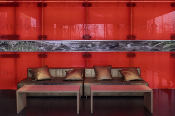 Sofa with golden cushions in front of a red-illuminated glass wall, stylish lobby of an apartment