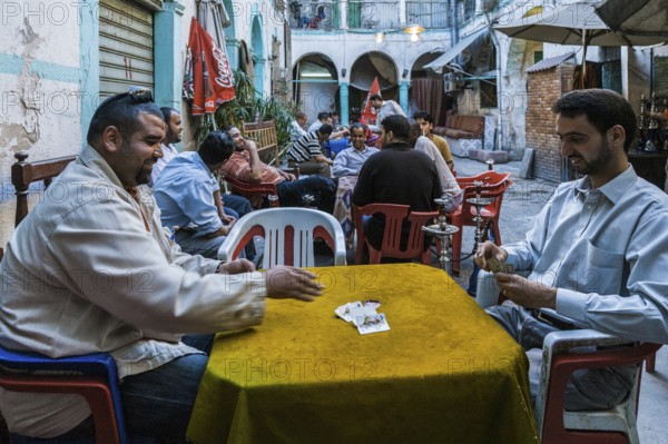 Tripoli, Libya, North Africa. Man playing cards and others smoking shisha in a traditional 'funduq'