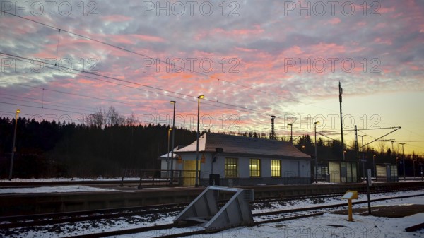 A small train station at dawn under a colorful sky with snow-covered ground, Rennsteig, Frankenwald