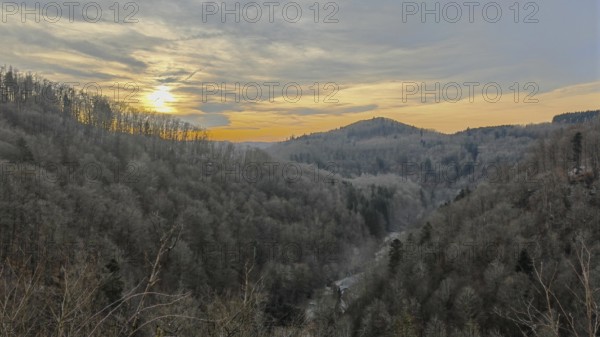View over the forest into a valley with trees in the light of a sunset and a fascinating sky,