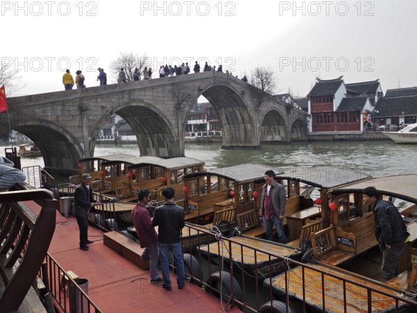 People on a stone bridge admire the wooden boats on the river in a historic city setting,