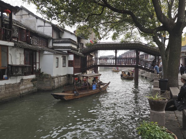 Traditional bridge over a canal with boats flanked by old houses and trees, Zhujiajiao Ancient