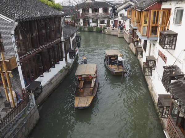 Two boats sail through a narrow canal lined with traditional Chinese buildings, Zhujiajiao Ancient