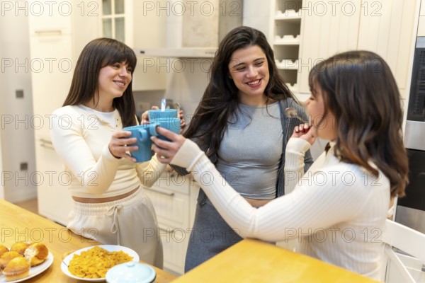 Young friends clinking coffee mugs and laughing in a modern kitchen, enjoying breakfast with cereal