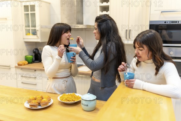 Three smiling young women sharing muffins and cereal, laughing and chatting over breakfast in a