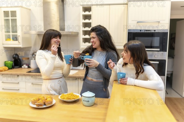 Three smiling young women friends enjoying breakfast together, eating cereal and muffins, drinking