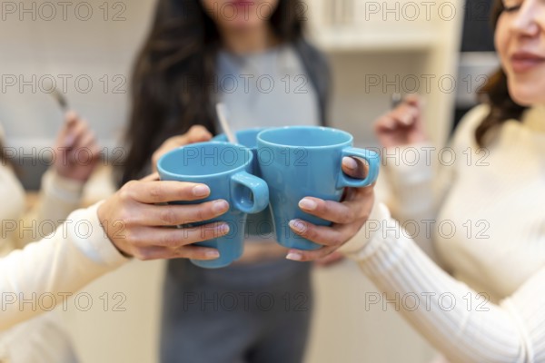 Close up of friends clinking bright blue mugs together in a warm kitchen, celebrating friendship