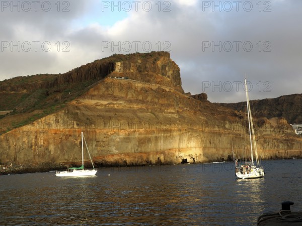 Rocks on calm sea with boats and golden evening sun, Puerto de Mogan, Gran Canaria, Canary Islands,