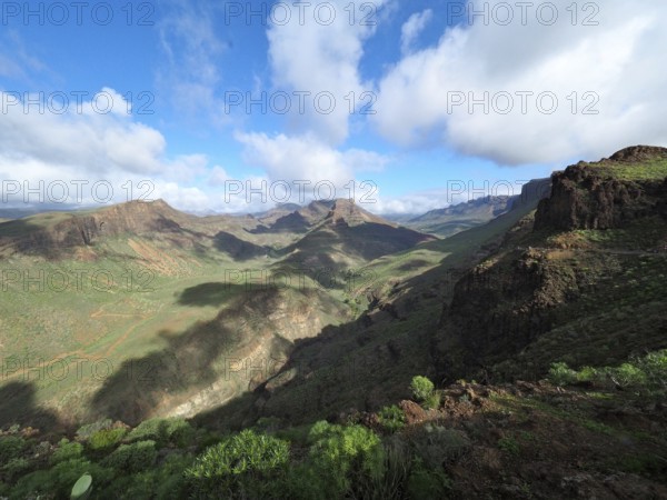 Wide mountain landscape with green valleys and dramatic cloudy sky, Barranco de Fataga, Gran