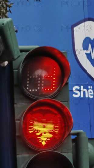 Traffic light shows red light with Tiran flag eagle against blue background in an urban