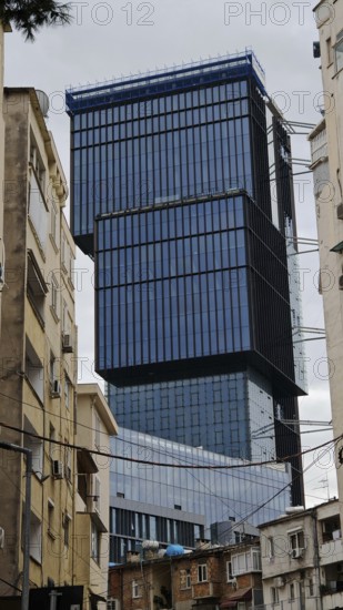 Modern high-rise building with glass façade between older buildings in an urban environment under