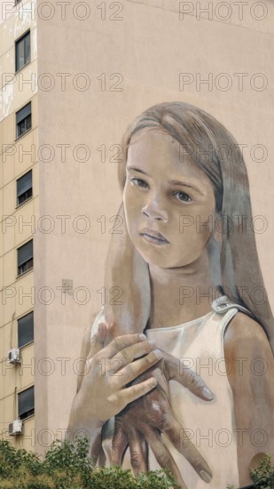 Large mural of a thoughtful girl on the façade of a building with natural facial expression,