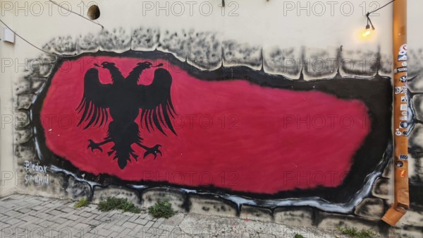 Graffiti depicting the flag of Albania with a black eagle on a red background on a wall along a