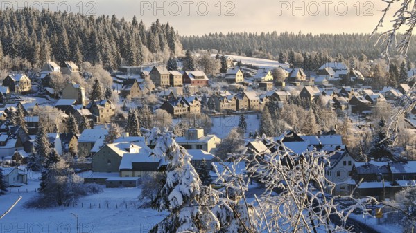 Snowy village in front of wooded hills under blue skies, Rennsteig, Thuringian Forest nature park
