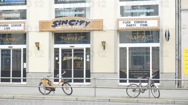 Club façade with posters and two bicycles in the foreground and sign Fuckcorona during corona,