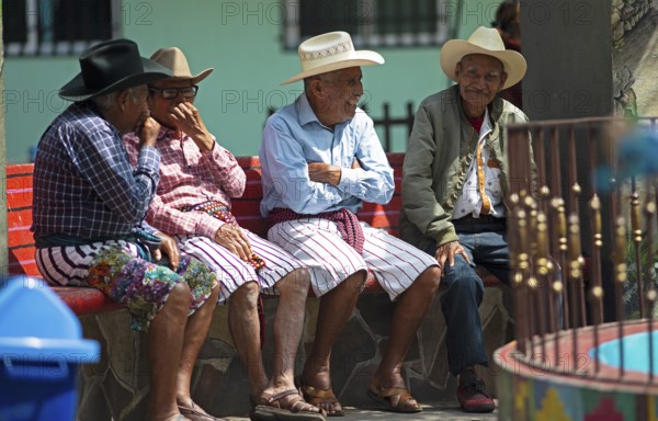 Guatemalan men wearing Coxboy hats sitting laughing on a bench in Santiago de Atitlán, Sololá