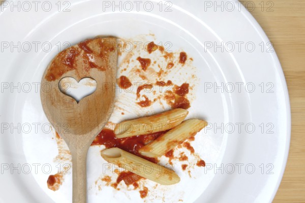 Plate with cooking spoon and leftovers from pasta, food waste