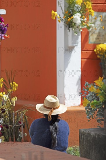 Mayan woman wearing straw hat looking at a colorful grave in the cemetery in Chichicastenango,