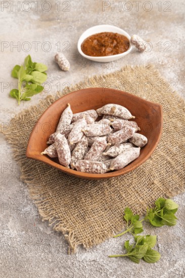 Small smoked Chicken sausages in clay bowl on brown concrete background and linen textile. side