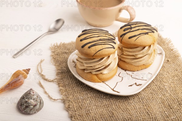 Caramel Cream Cakes on white wooden background and linen textile, cup of coffee, side view, close