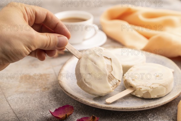 ?hocolate Ice cream in white glaze, cup of coffee, with hand on brown concrete background and