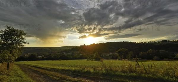 A rural scene with meadows and dirt roads at sunset, dramatic cloud formations, Franconian Forest