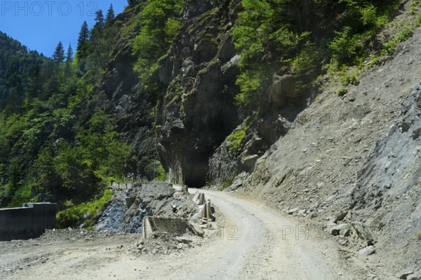Gravel road winds around rocky mountain walls near a tunnel, road 7 partly slipped down, west of