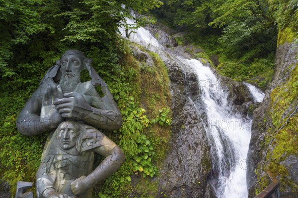 Sculpture in the forest next to a rushing waterfall, statue of Saint Andrew and waterfall of Saint