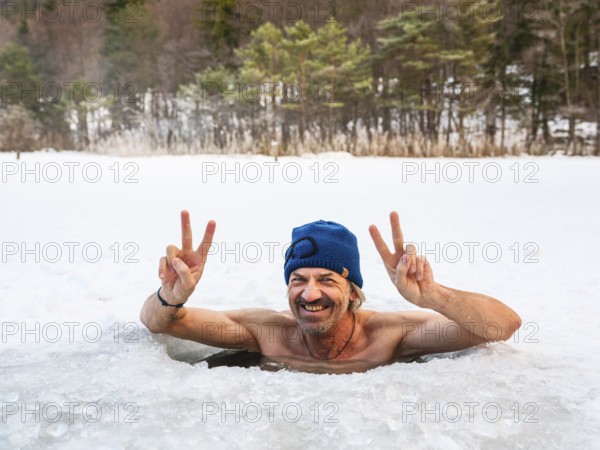 Man with cap, 55, ice bathing in an ice hole makes the Victory sign with both hands, Thumsee, Bad