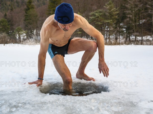 Man with cap, 55, climbs into an ice hole for ice bathing, Thumsee, Bad Reichenhall,