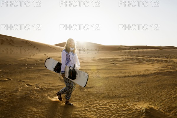 Young woman with snowboard in the sand dunes, near Merzouga, Meknès-Tafilalet region, Erg Chebbi,