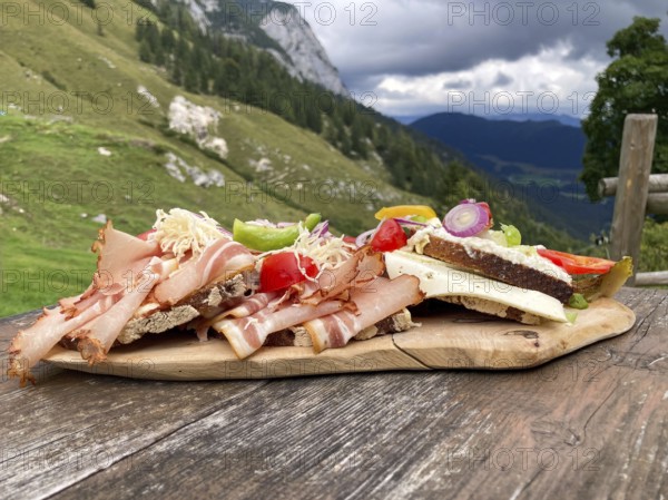 Typical snack on the alpine pasture, bacon bread and cheese bread on wooden plate on wooden table,